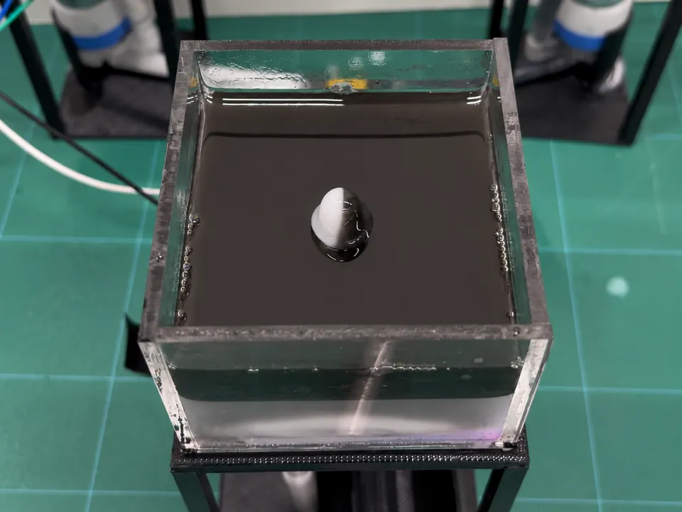 Black-and-white liquid pixel rising from the center of a dark liquid surface